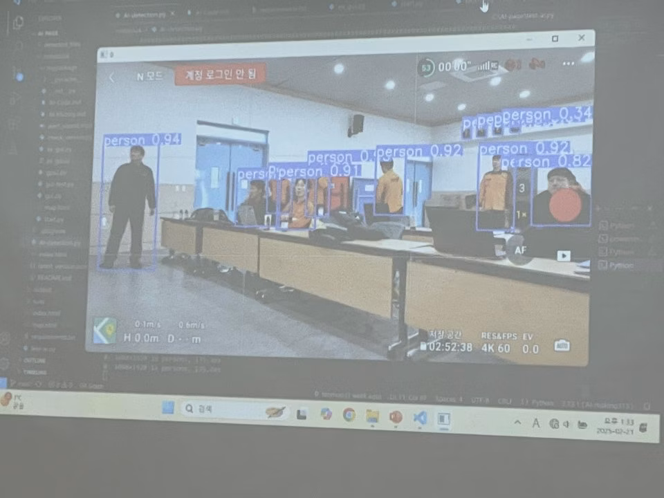 강의실 스크린의 실내 드론 영상에서 여러 사람 후보에 탐지 상자가 표시된 모습